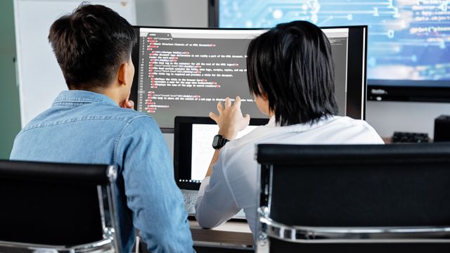 Two developers reviewing code together on a desktop monitor