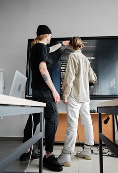 Two young adults collaborating on a coding project in a modern office setting.