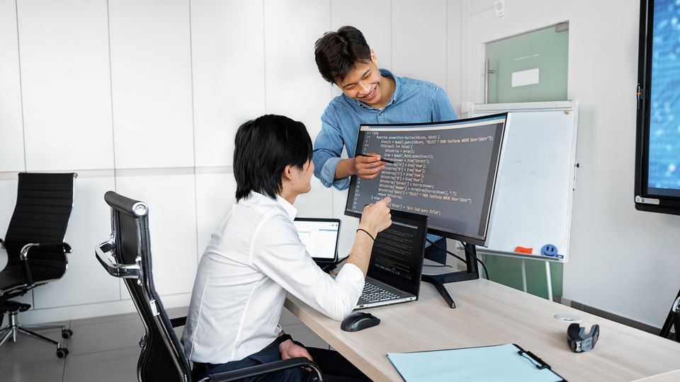 An Asian engineer walking a new team member through their setup on a monitor.