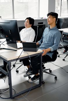 Two young men collaborating at computers in a modern workspace.