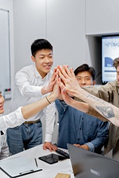 A group of young professionals high-fiving during a collaborative office meeting symbolizing teamwork and unity.