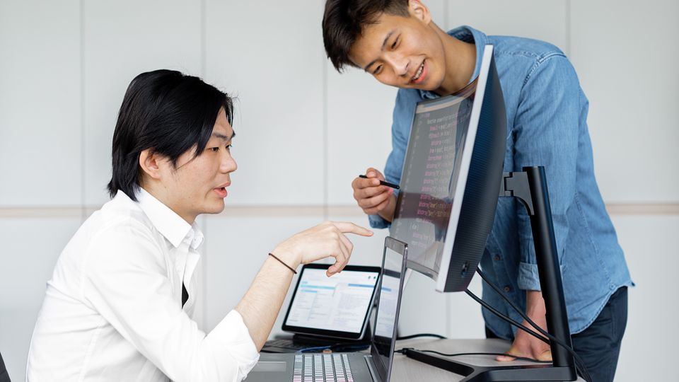 Two Asian engineers standing at a monitor together during a quick working session.