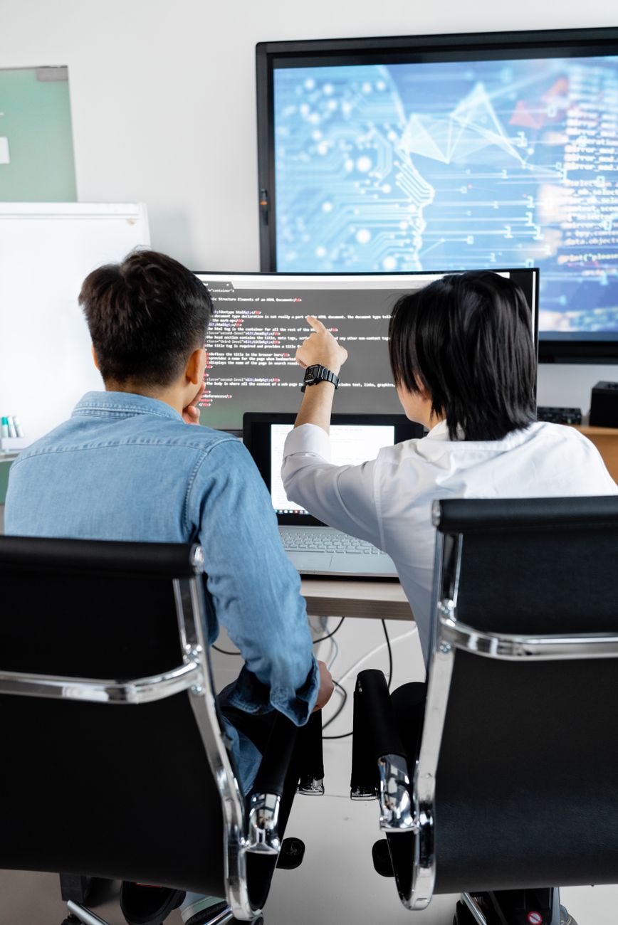 Engineers reviewing code changes on a shared monitor before pushing them to production.