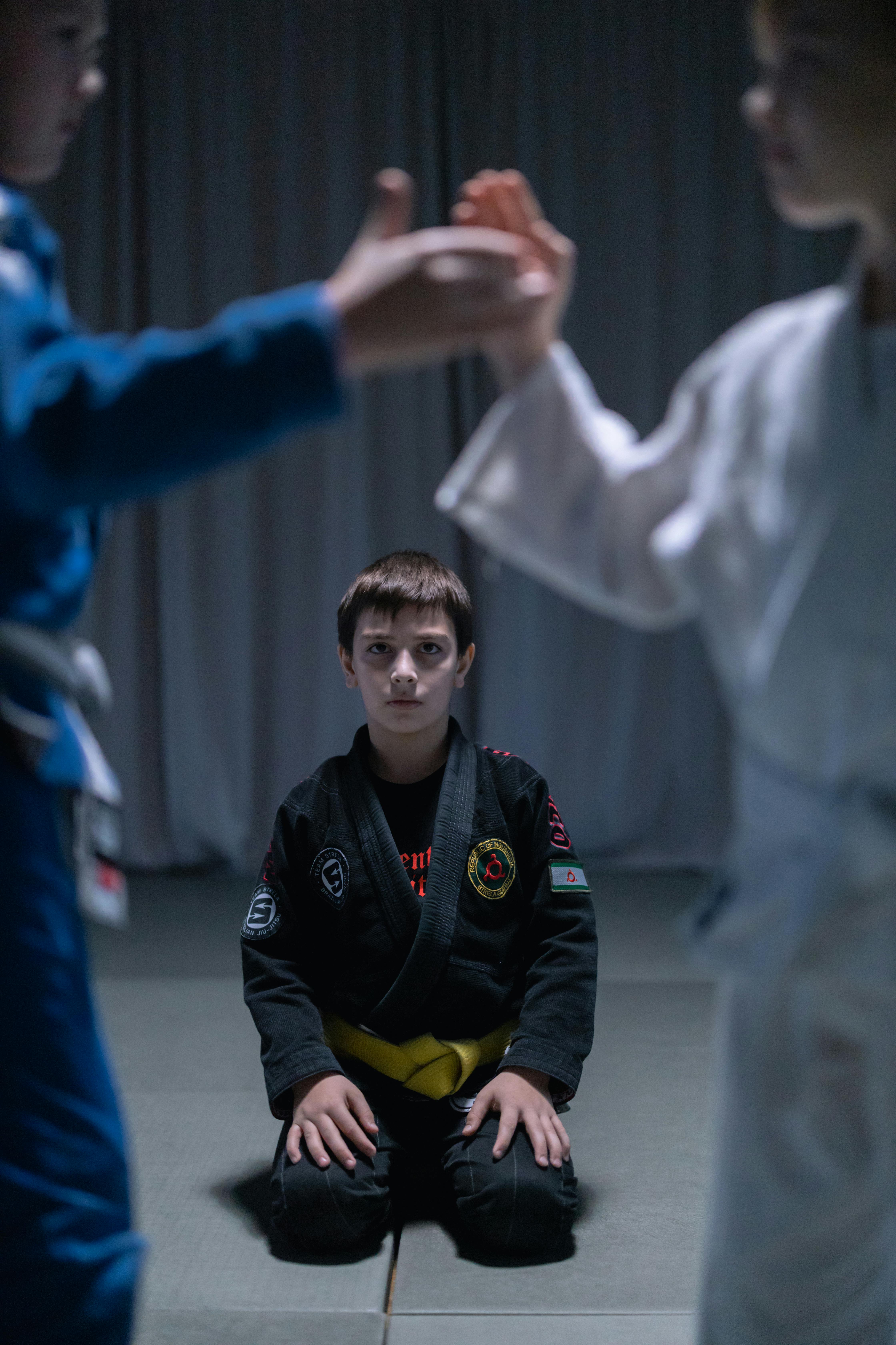 a boy in black gi sitting on black mat