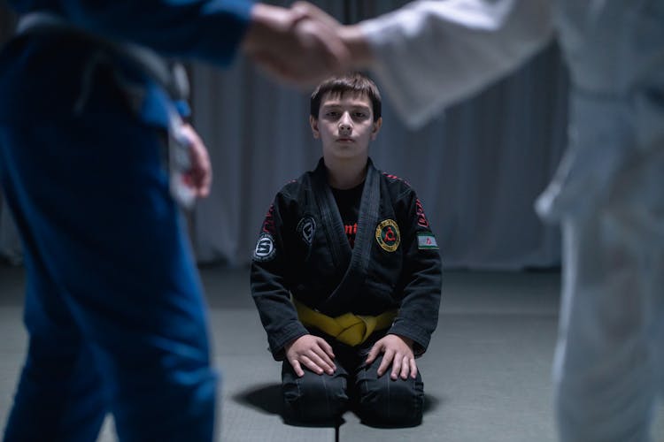 A Boy In Black Gi Kneeling On Black Mat