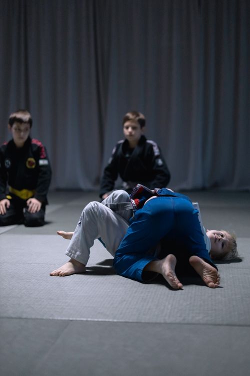 Free Young boys wearing gis practicing Jiu Jitsu grappling moves indoors. Stock Photo