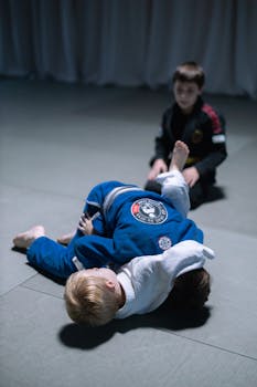 Children practicing jiu-jitsu indoors, demonstrating sportsmanship and martial arts skills on a rubberized mat.