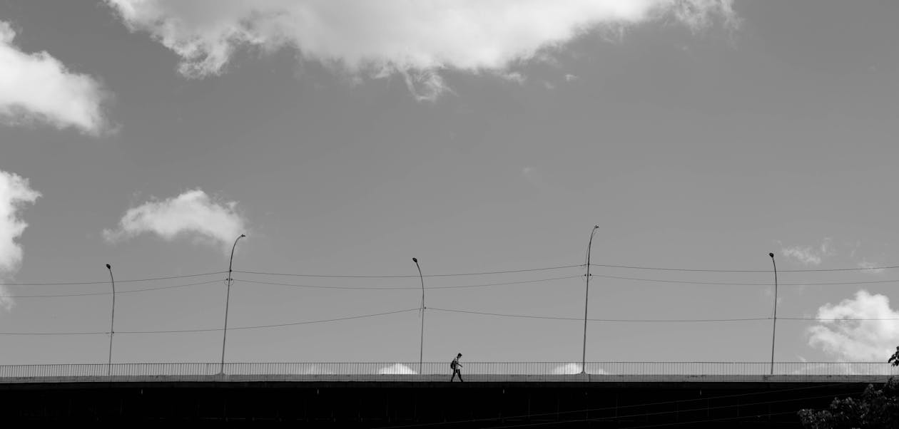 Grayscale Photo of a Person Walking on a Bridge