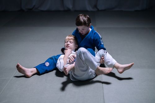 Free Two boys engage in grappling practice wearing judo uniforms on a mat indoors. Stock Photo