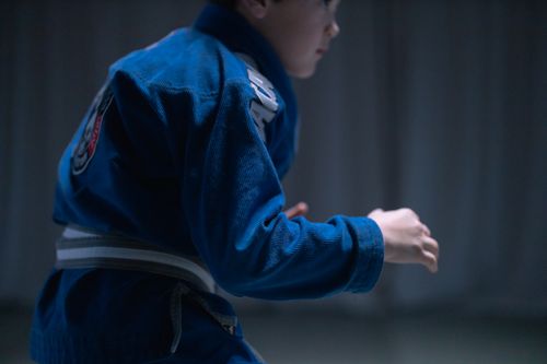 Free A young boy in a blue gi practicing Brazilian Jiu-Jitsu indoors. Stock Photo