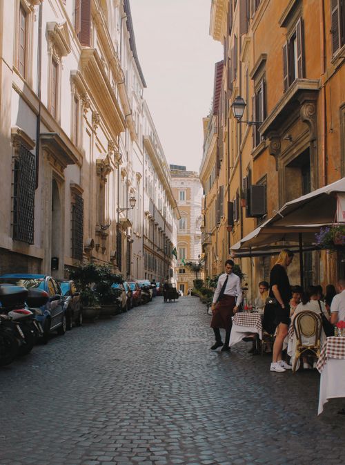 Free Quaint cobblestone street in Rome featuring a bustling sidewalk cafe. Perfect urban exploration scene. Stock Photo