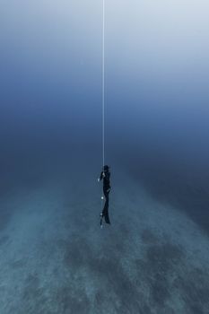 Anonymous diver in flippers and snorkeling equipment holding rope in dark blue seawater