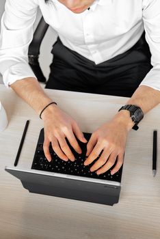 Top view of a man typing on a digital tablet with a keyboard on a wooden desk.