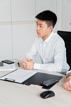 Asian man seated at desk in office, ready for a business meeting.