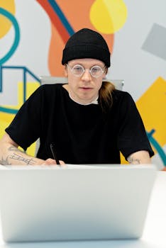 Focused young man in black beanie at laptop, modern workspace.