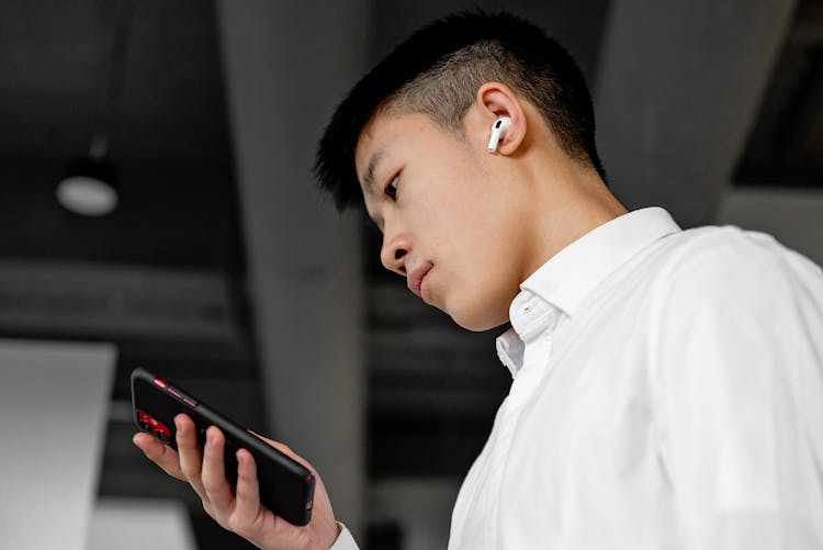 A Man Using Cellphone And A Wireless Earphone