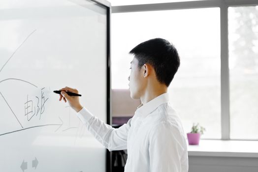 Side view of an Asian man writing on a smart whiteboard in a modern office setting.