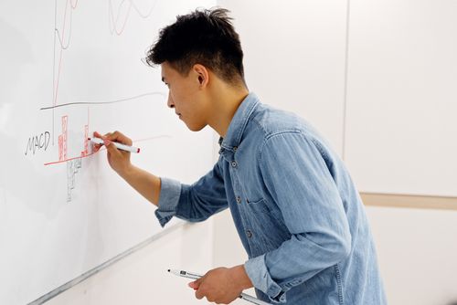 Free Side view of an adult man writing on a whiteboard focusing on technical analysis and charting. Stock Photo