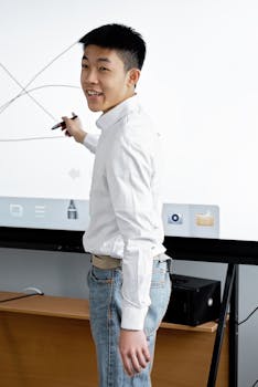Asian man smiling while explaining concepts on a digital whiteboard, showcasing interactive presentation skills.