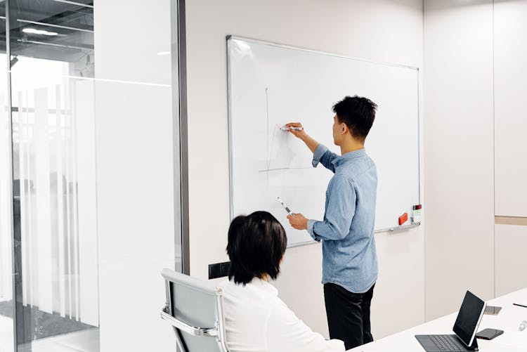 A Person In Smart Casual Attire Drawing On A Whiteboard