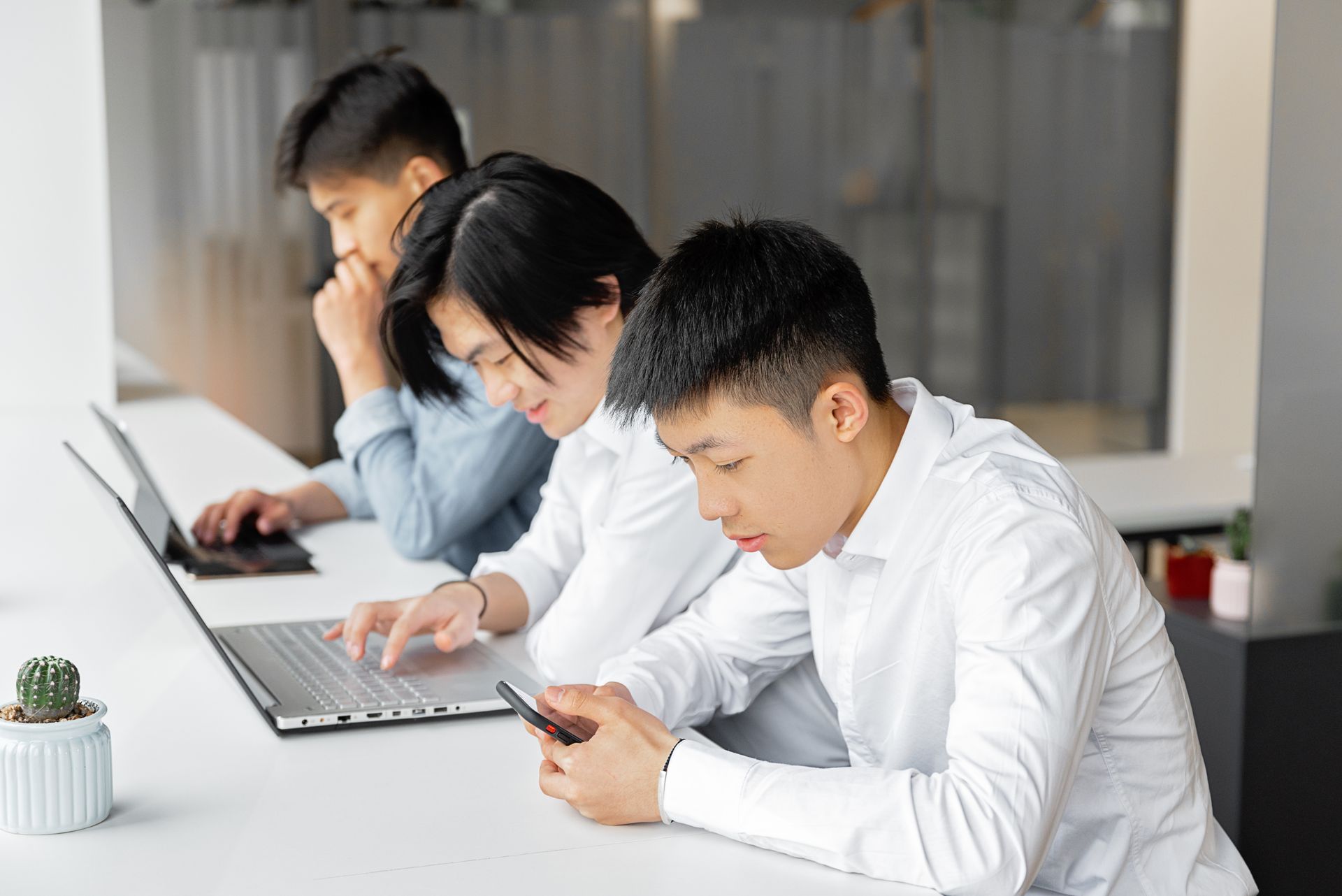 Three young professionals using technology collaboratively in a modern office setting.