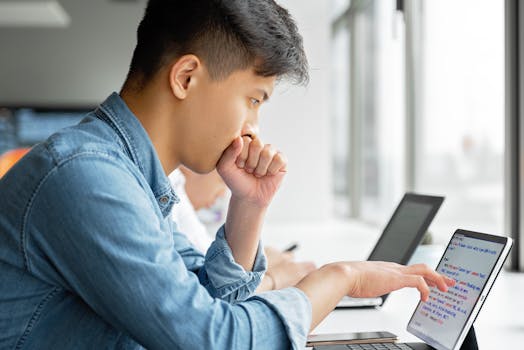 Asian man deeply engaged in work on a laptop at a contemporary workspace, side view.