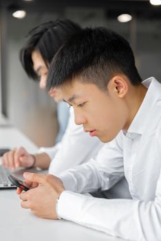 Two Asian men focused on smartphone usage in a modern indoor setting.