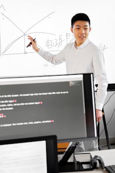 An Asian adult male in smart casual attire giving a presentation on an interactive whiteboard with graphs.
