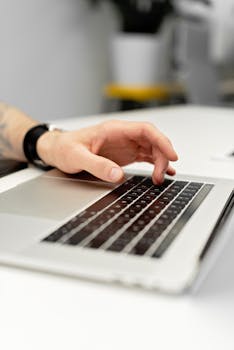 Close-up of a hand typing on a laptop keyboard at an office desk.
