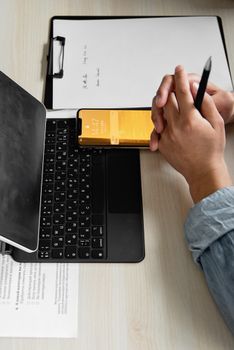 Close-up of hands working on a clipboard with a smartphone and laptop, ideal for business or tech themes.