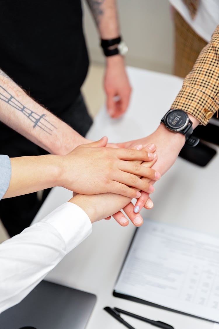 Close-up Of Coworkers Putting Their Hands Together Above The Desk With Documents 