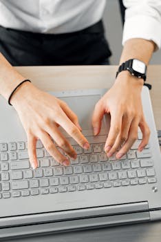 Close-up of hands typing on a laptop keyboard, captured from above.