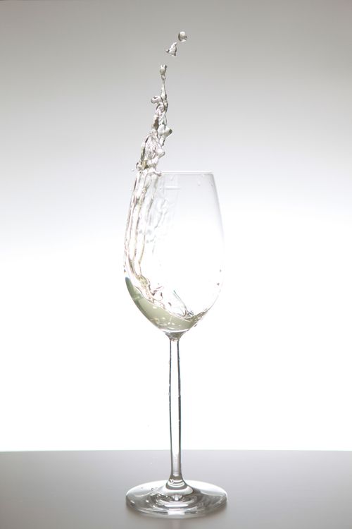 Free Crystal-clear wine glass with dynamic splash on clean white background. Stock Photo