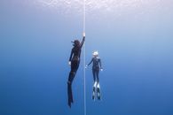 Full body of faceless people in diving suit and flippers with goggles swimming underwater in blue sea near rope in daytime
