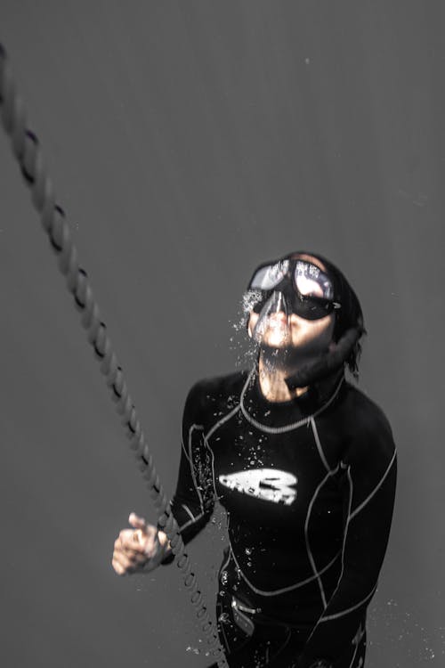 Anonymous person diving underwater near cable in sea
