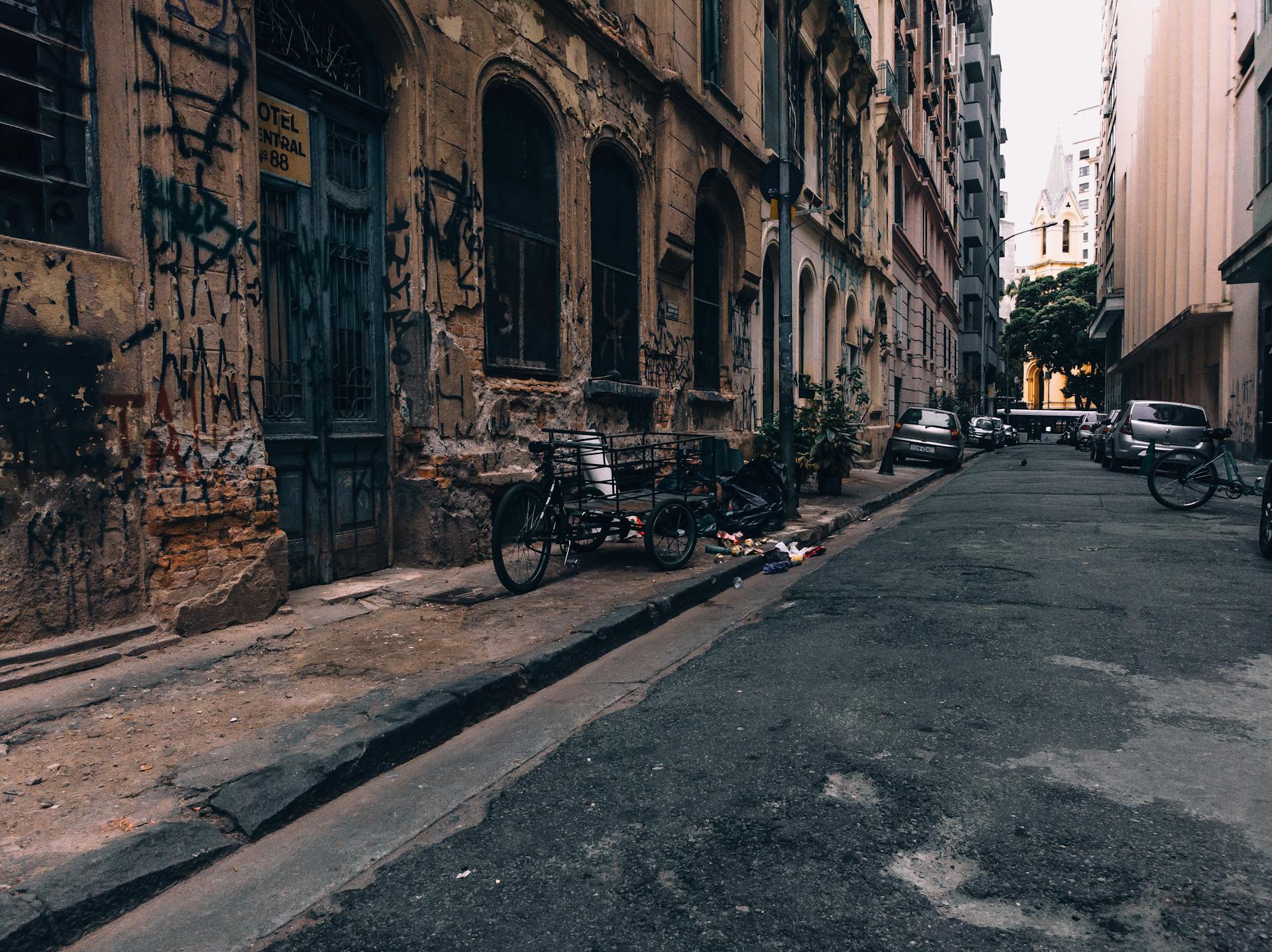 Bike with carriage and cars parked near old damaged buildings with vandal graffiti in alley