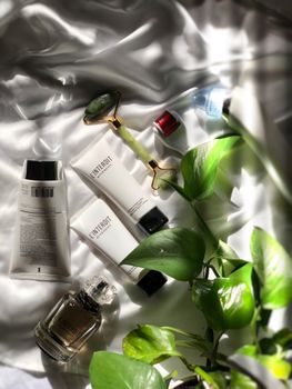 High-end skincare products and jade roller on silk with greenery