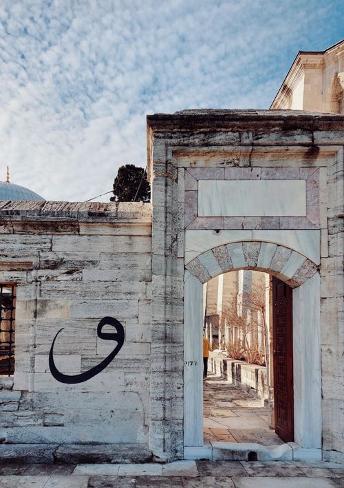 Free Stone walls with archway featuring Arabic calligraphy under a blue sky in a historic setting. Stock Photo