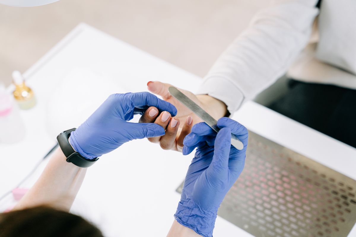 Close-up of a nail technician filing a client's nails with blue gloves in a professional setting.
