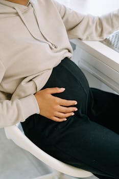 Close-up of a pregnant woman sitting on a chair, gently holding her belly.