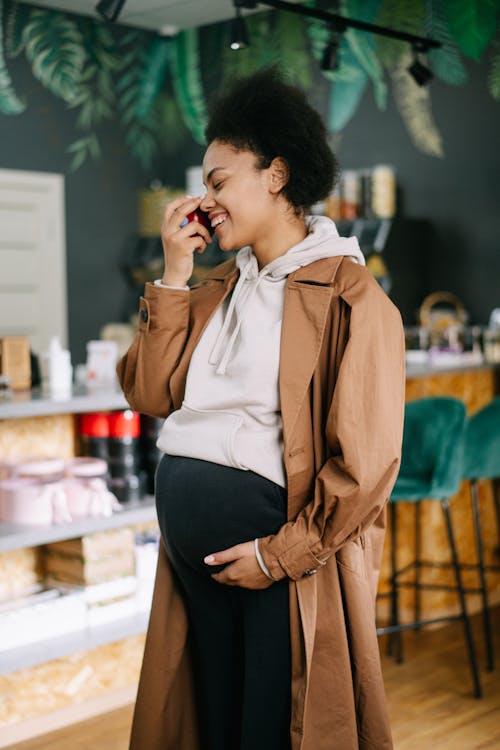 Pregnant Woman in Brown Trench Coat Holding a Red Fruit