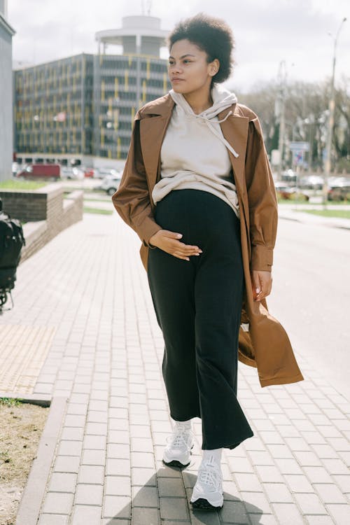 A Pregnant Woman Holding Her Baby Bump while Walking