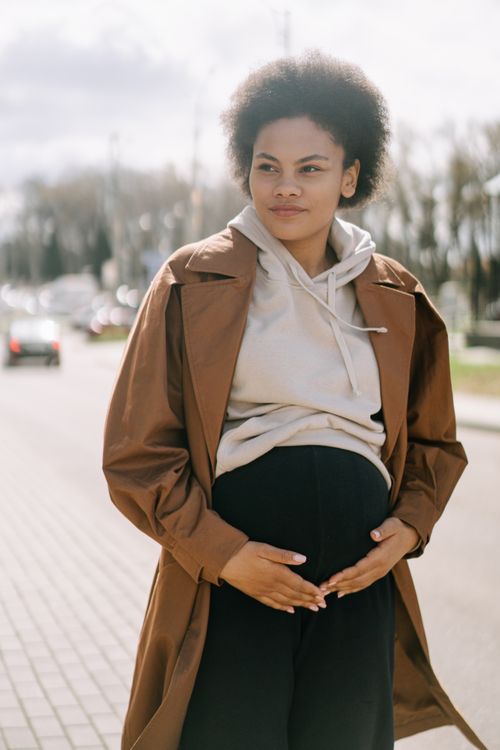 Free Pregnant woman in urban setting, hand on belly, reflecting motherhood and expectancy. Stock Photo