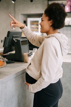 Expectant mother pointing at menu while ordering in a cafe. Casual and lively atmosphere.