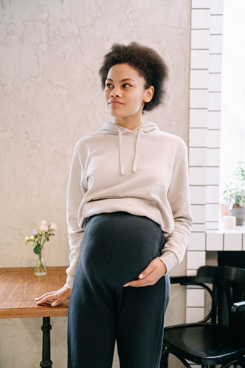 Free A pregnant woman with afro hair standing indoors, hand on belly. Stock Photo