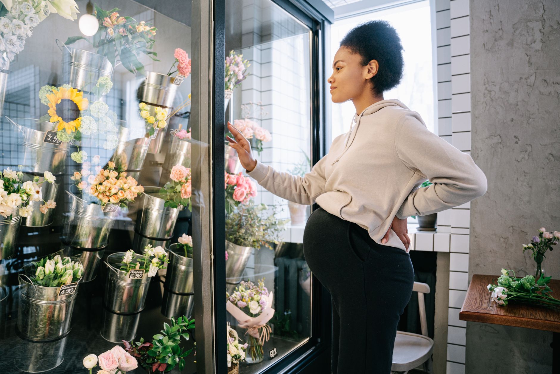 A pregnant woman stands indoors, admiring floral arrangements in a flower shop.