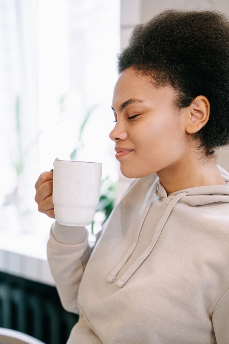 A Woman In Beige Sweatshirt Holding A Ceramic Mug