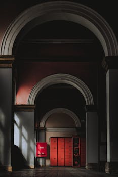 A mysterious indoor hallway featuring dramatic arches and red lockers, casting intriguing shadows.