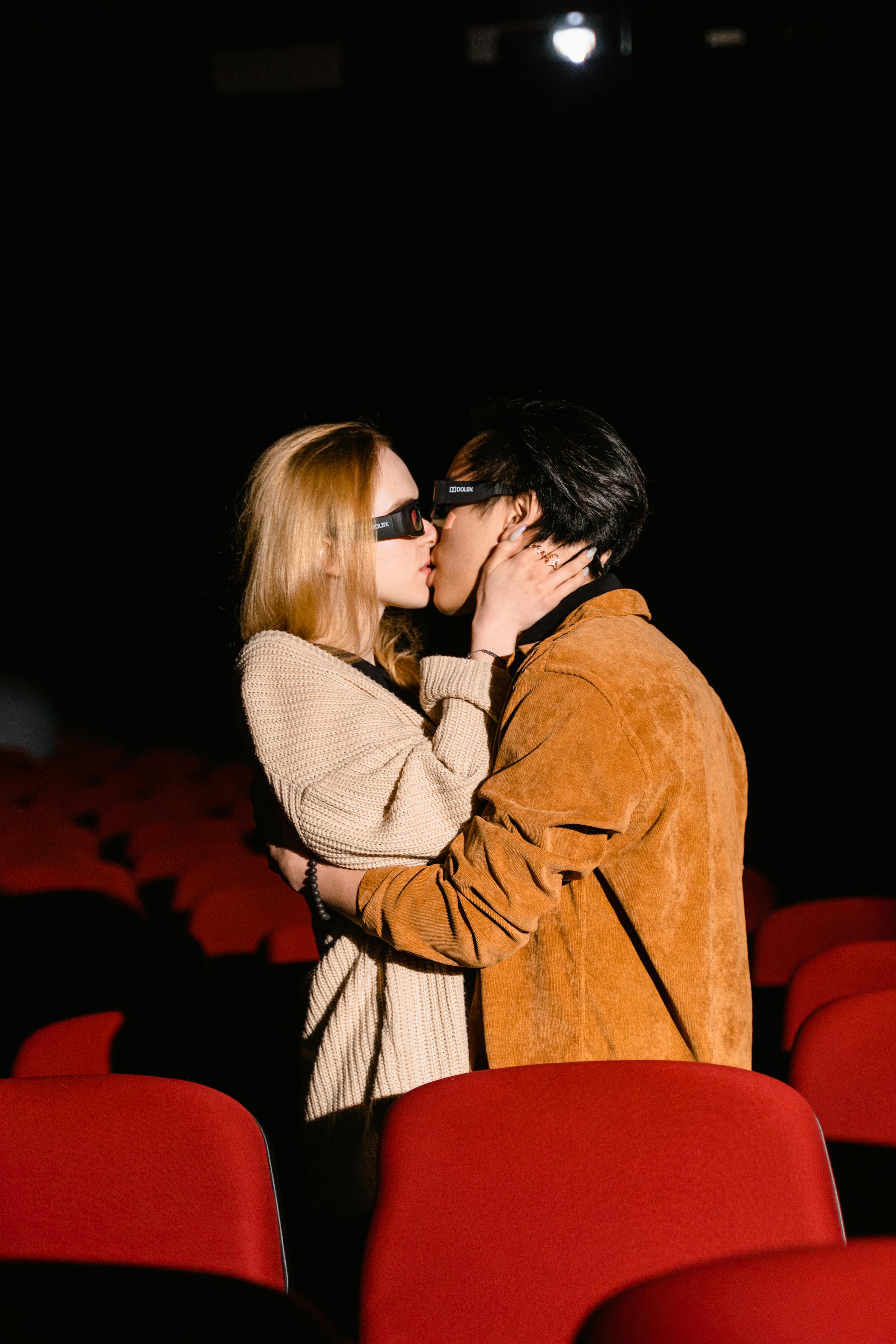 Free Couple kissing passionately in a dimly lit cinema, embracing love and intimacy. Stock Photo