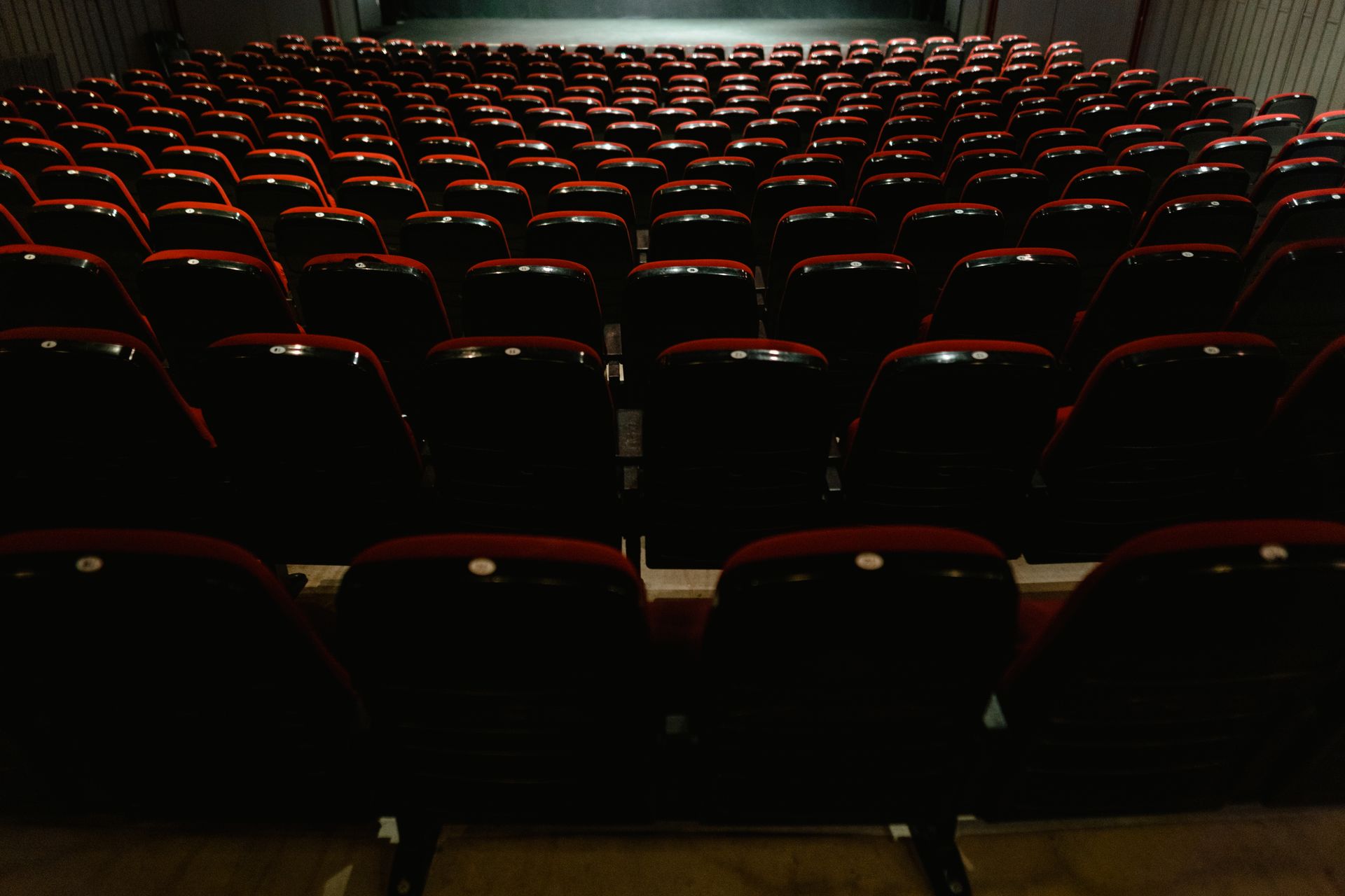 An empty movie theater interior with rows of red and black seats, awaiting audience.